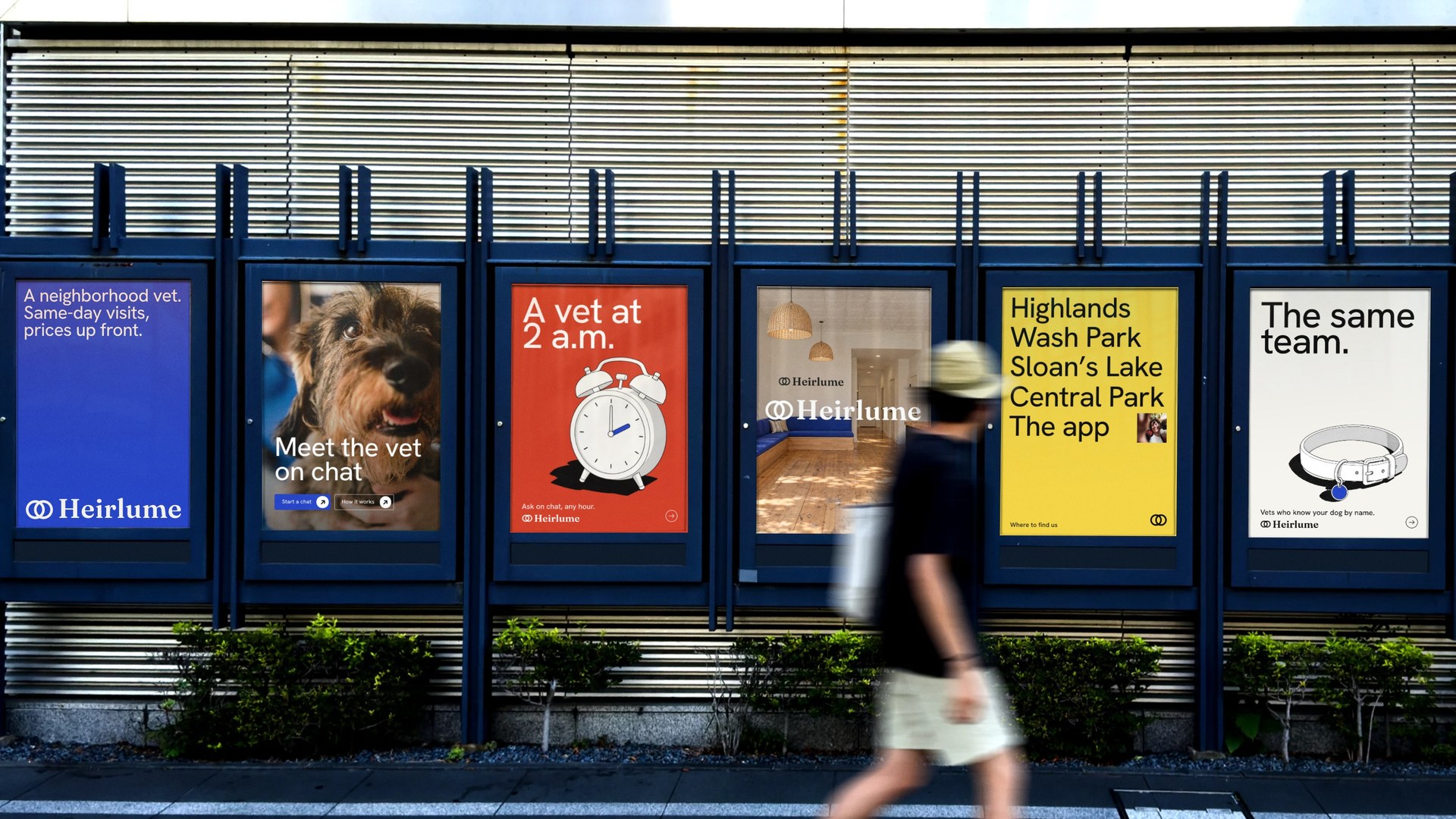 A wall of Heirlume posters on a city street, a man walking past