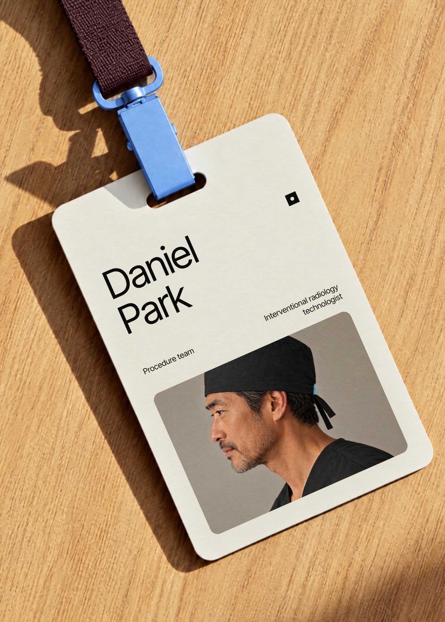 A Minimal Clinic staff badge on an oak table, plum strap and cornflower clip